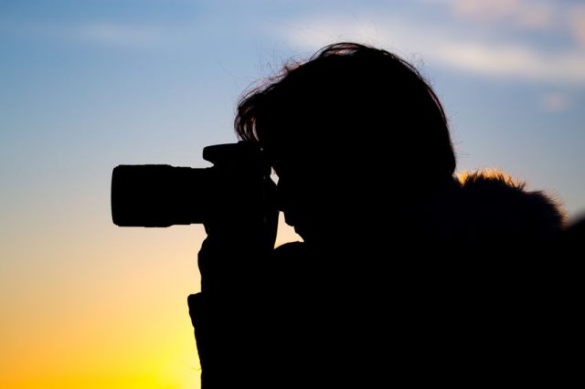 A girl is taking pictures with a camera at sunset .
